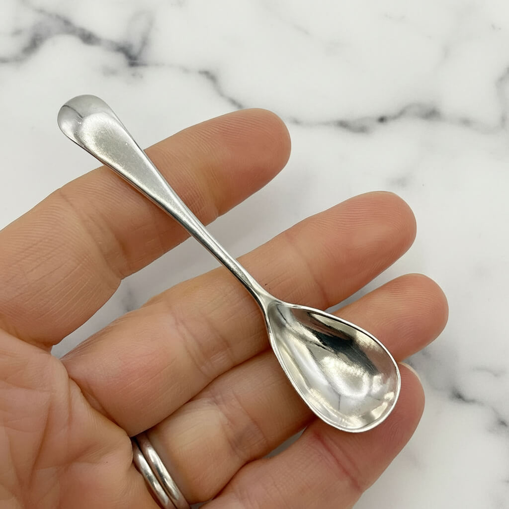 Silver spoon held between fingers against a marble background