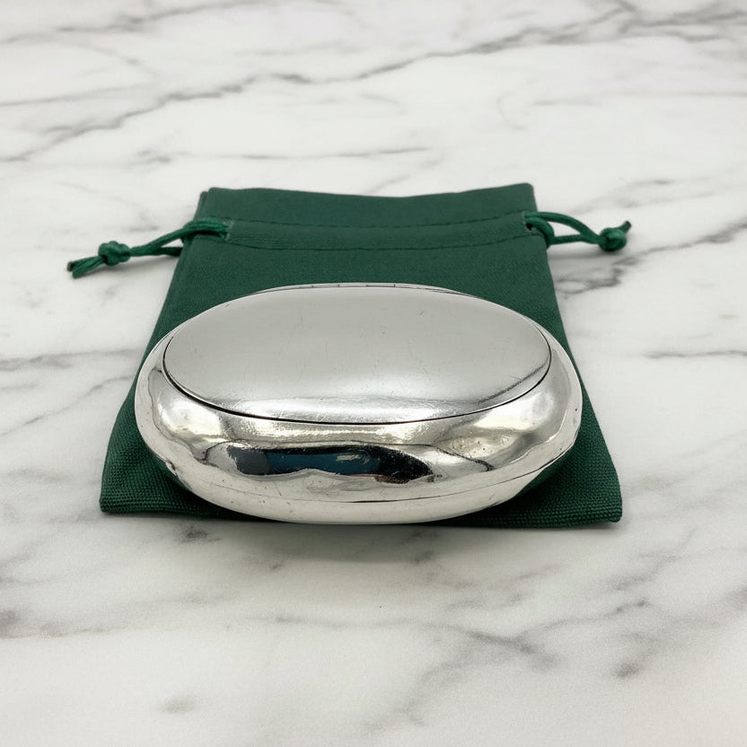 Silver oval box on a green drawstring bag with a marble background