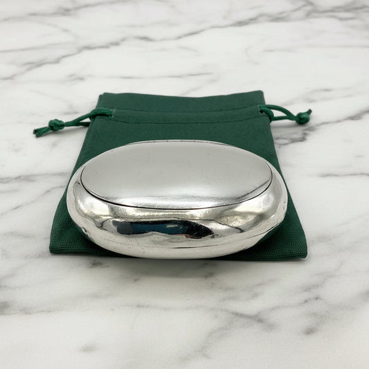 Silver oval box on a green drawstring bag with a marble background