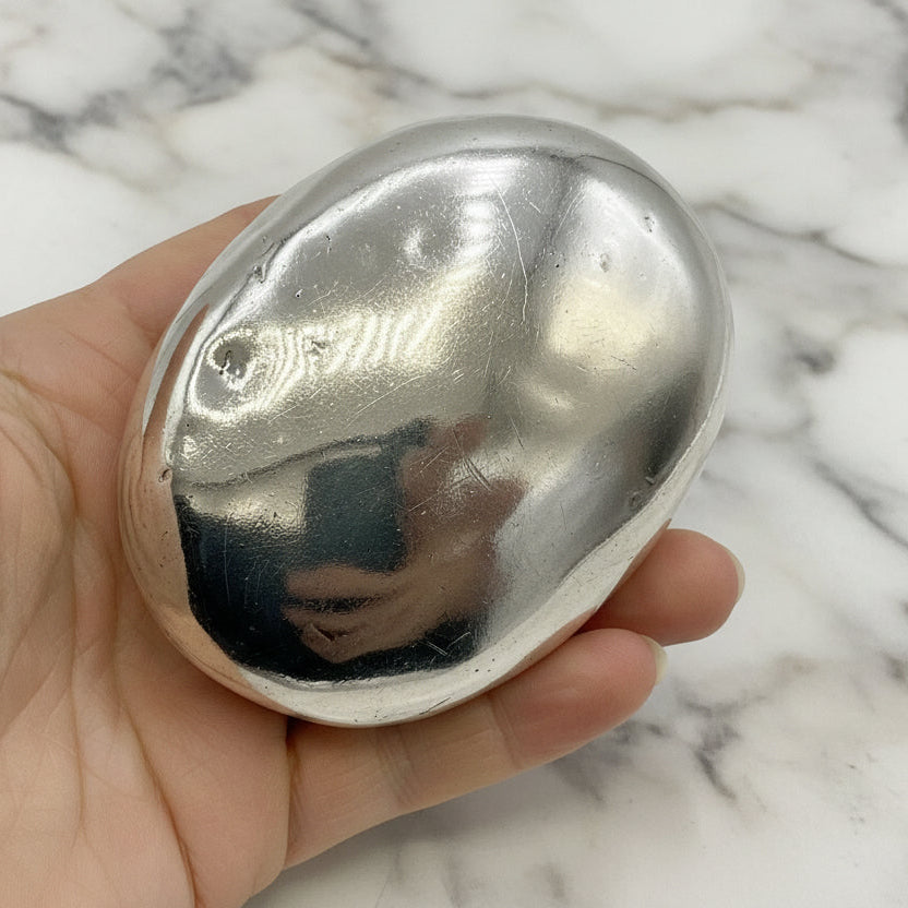 Base of silver oval box held in a hand against a marble background