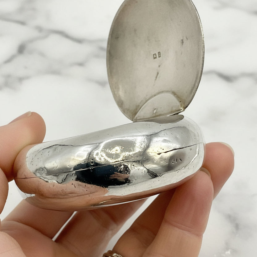 Side view of silver oval box held in a hand with a marble background
