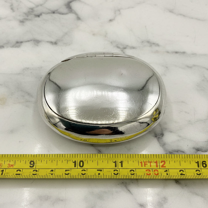 Silver oval box on a marble surface with a measuring tape for scale.