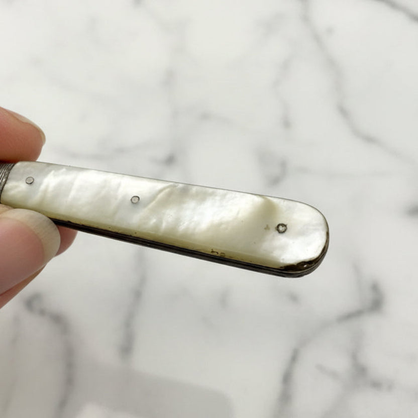 Hand holding a small fruit knife with a pearl handle against a plain background