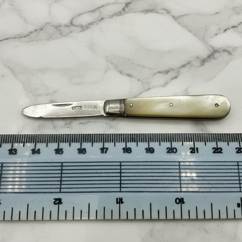 Small knife with a pearl handle next to a ruler for scale on a marble background