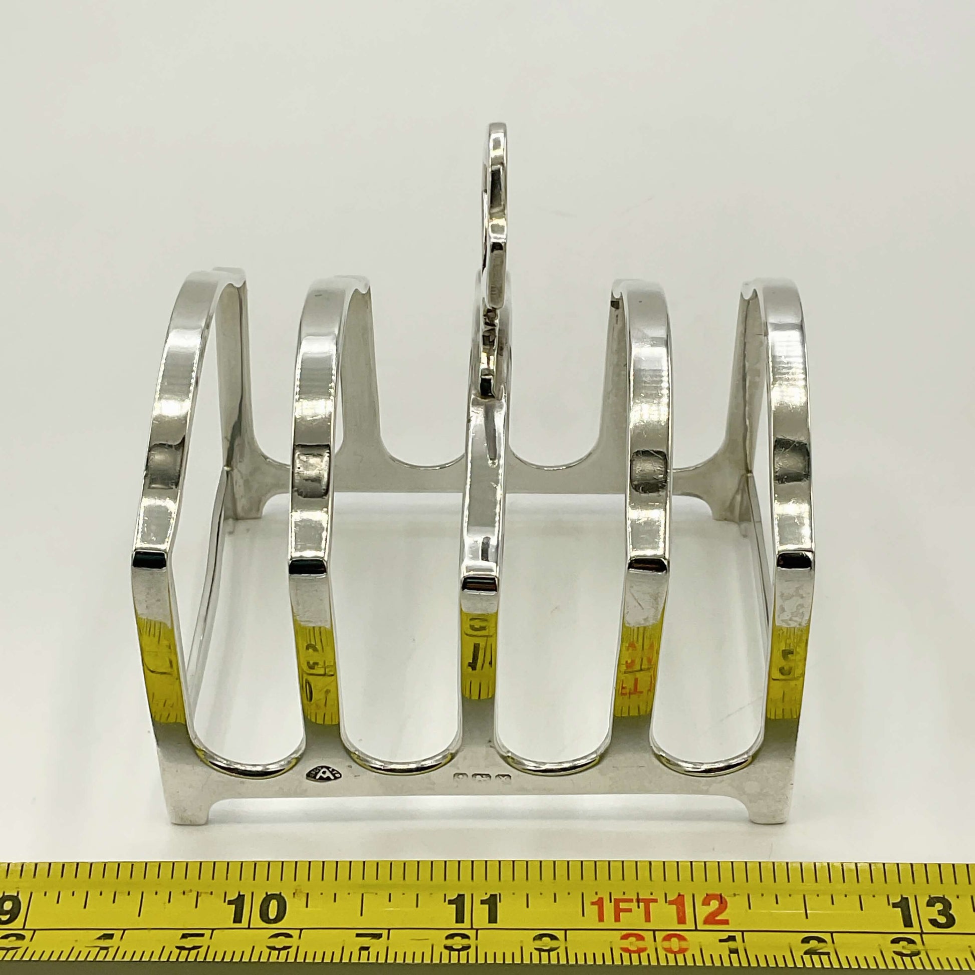 Silver toast rack with measuring tape for scale on a white background