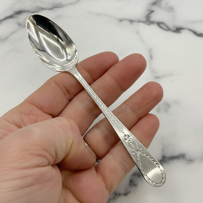 Silver spoon held in a hand against a marble background