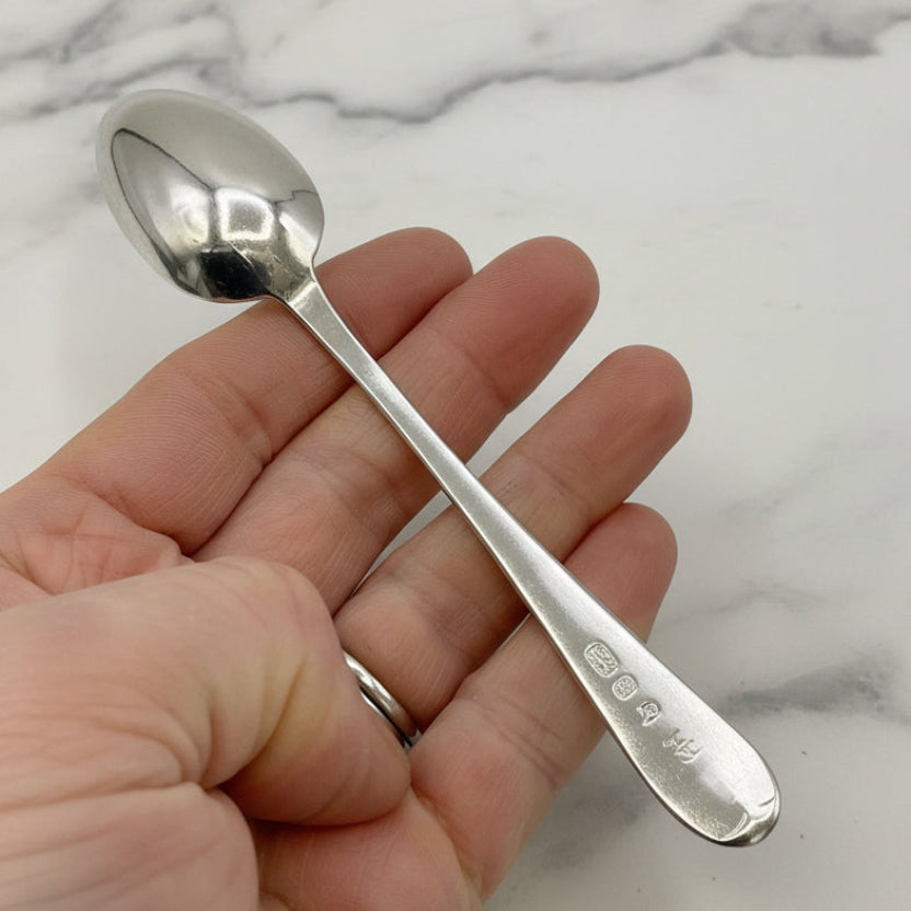 Silver spoon held in a hand against a marble background