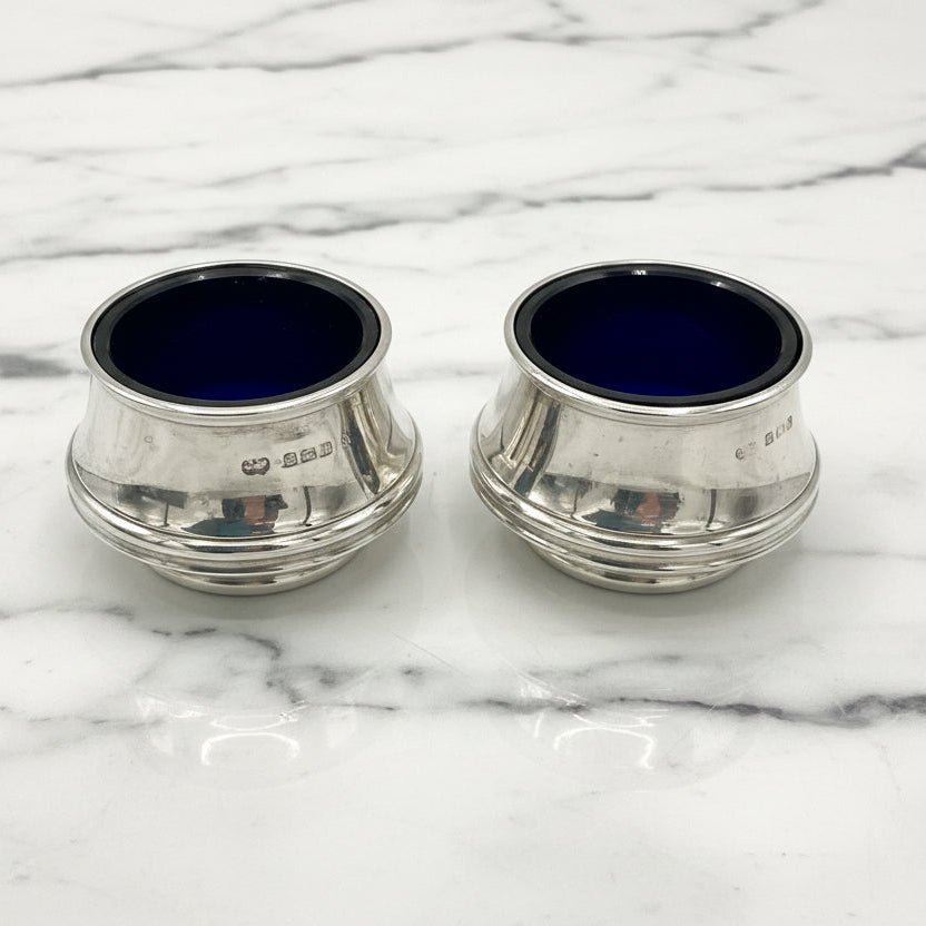 Two silver salts with blue liners on a marble surface