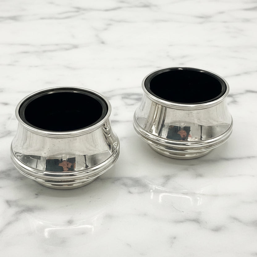 Two silver salts with blue liners on a marble surface