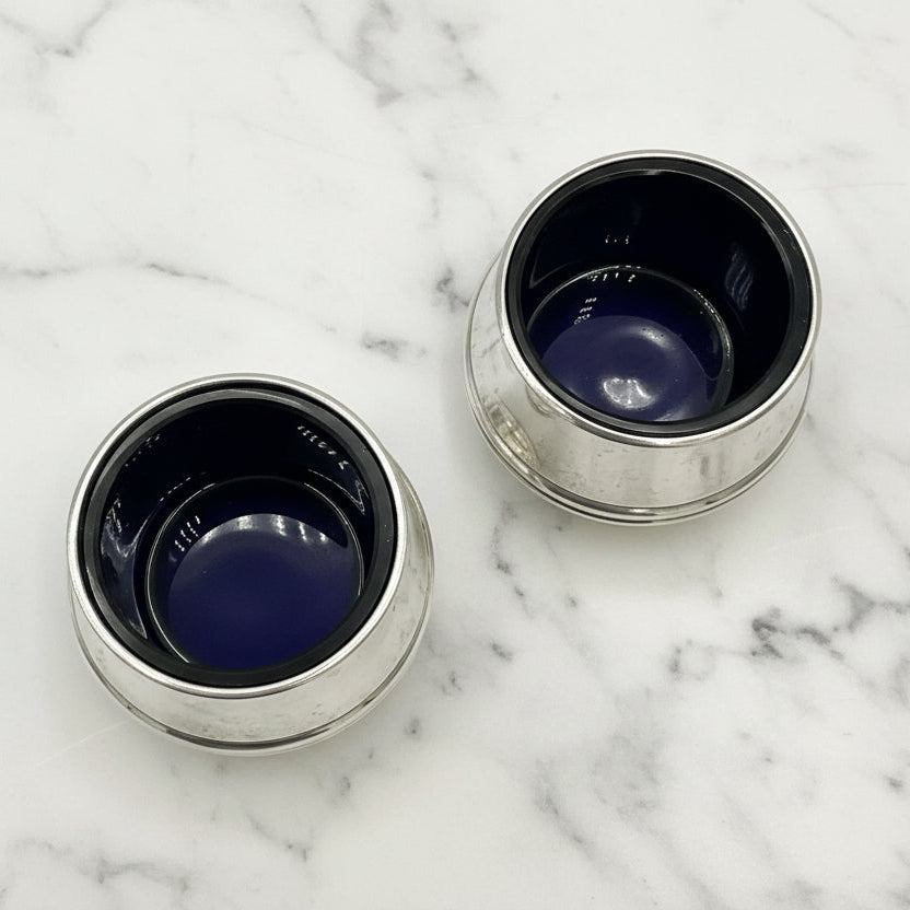 Two silver salts with blue liners on a marble surface