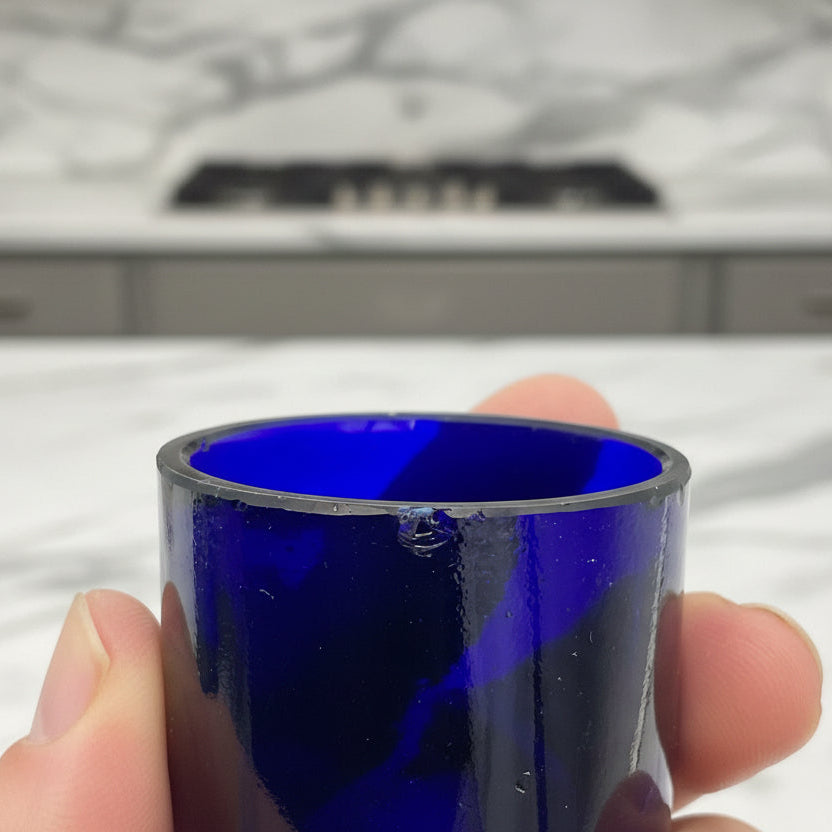 Hand holding a blue glass liner with a small chip against a marble kitchen background