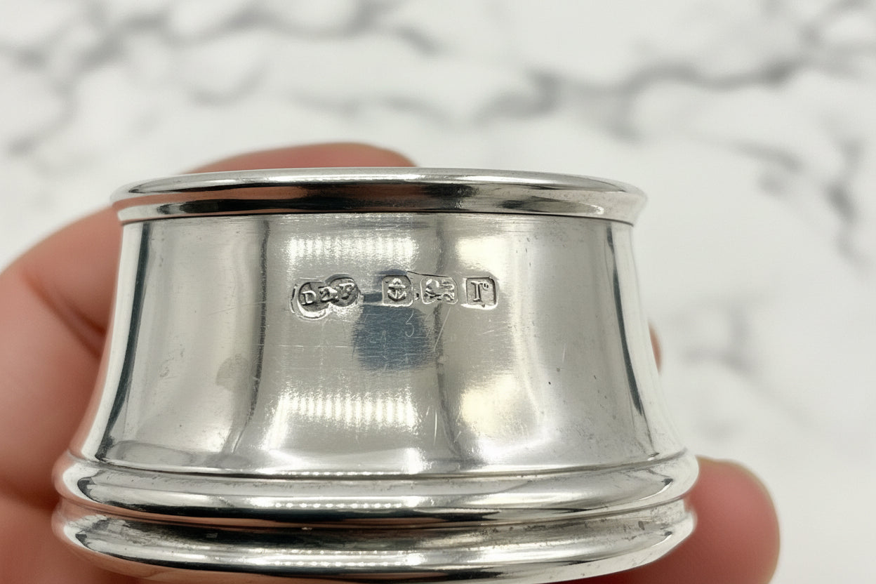 Silver salt held in a hand showing antique hallmarks with a marble background