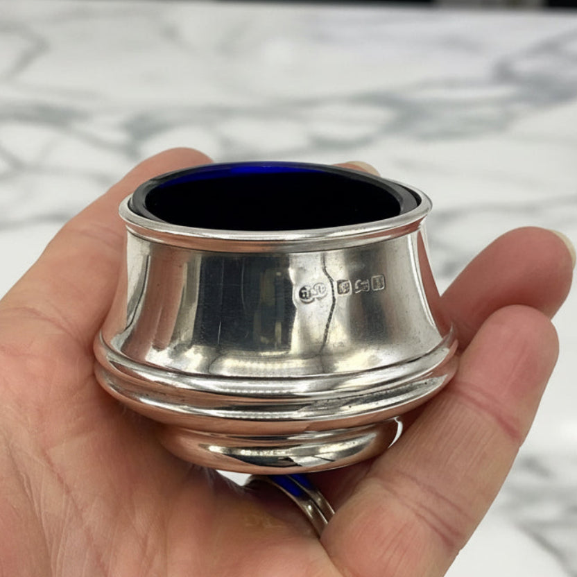 Silver salt with blue liner held in a hand against a marble background
