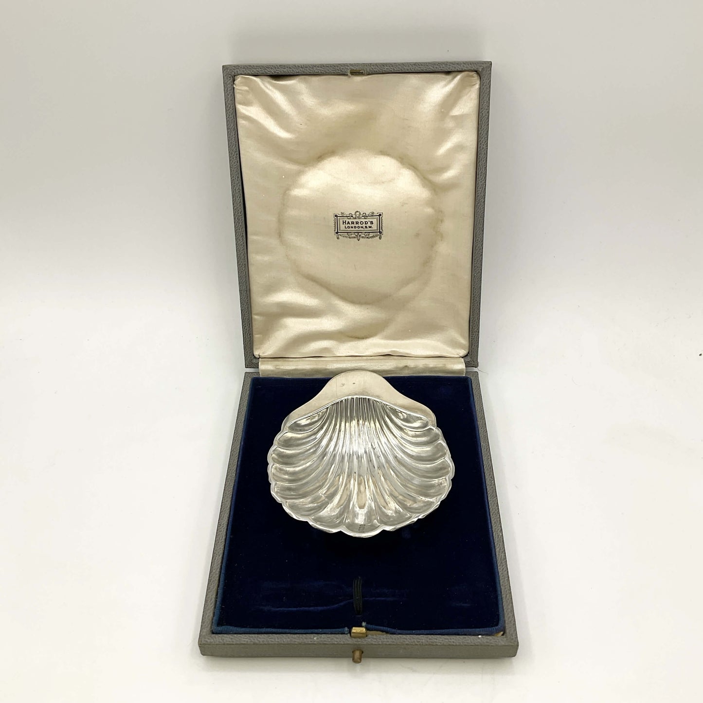 Silver shell-shaped object in a box on a marble surface