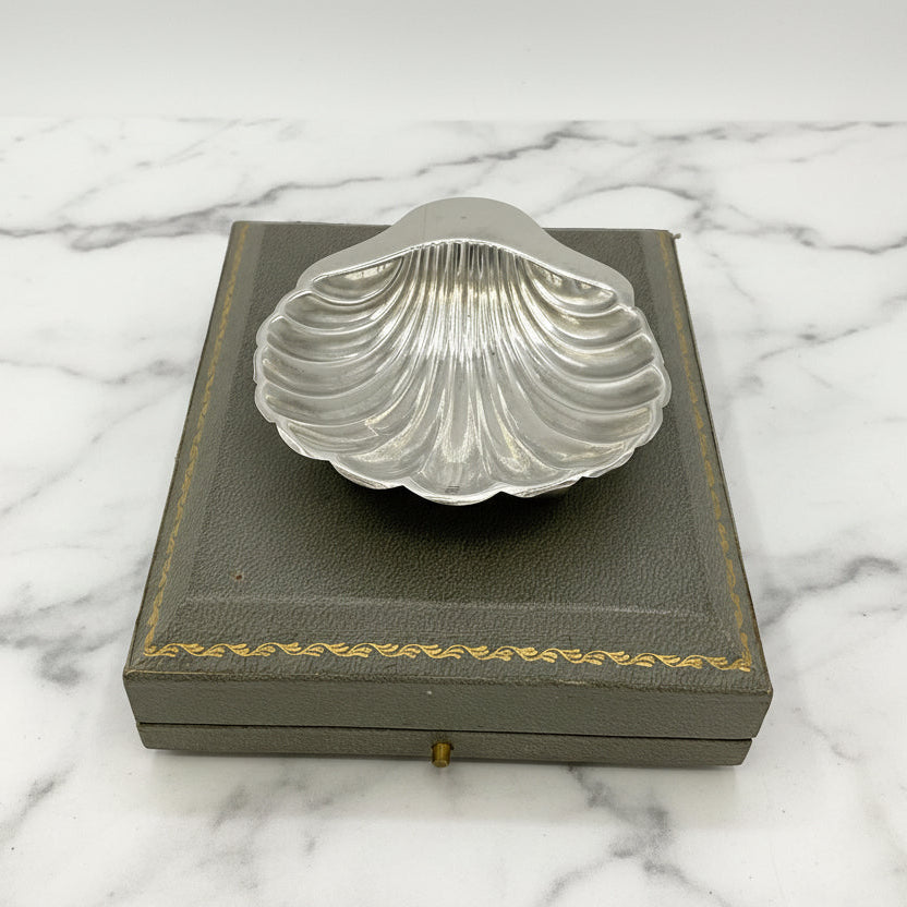 Silver shell-shaped dish on a grey box with gold trim and marble background 