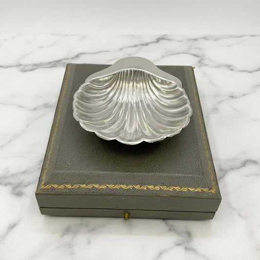Silver shell-shaped dish on a grey box with gold trim and marble background 