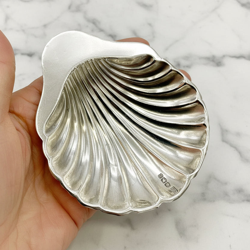 Silver shell-shaped dish held in a hand on a marble background