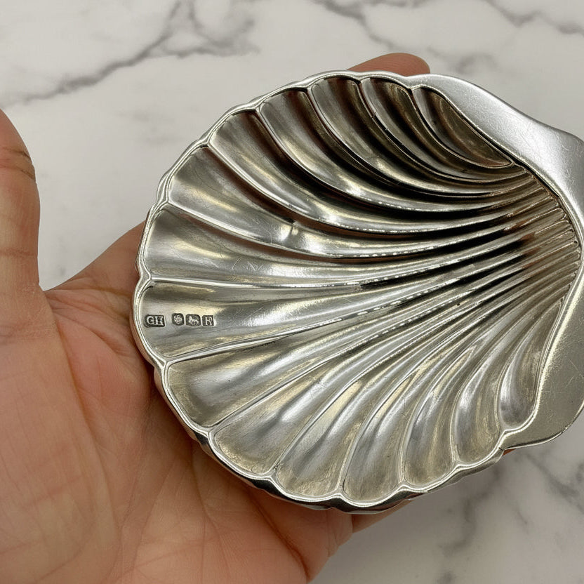 Silver shell-shaped dish held in a hand against a marble background