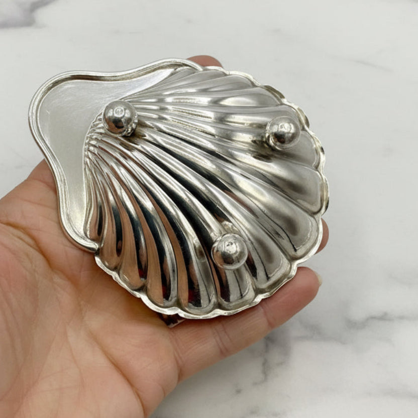 Silver shell-shaped dish upside down held in a hand against a marble background