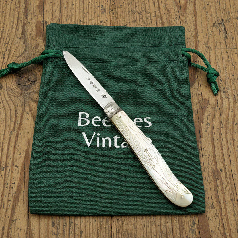 Antique fruit knife with decorative handle on a green drawstring bag labeled 'Beeches Vintages' on a wooden surface.