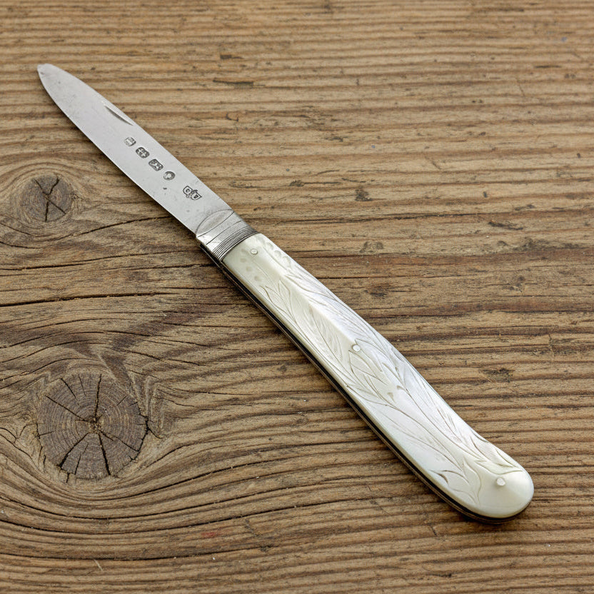 Pocket knife with decorative white handle on a wooden surface
