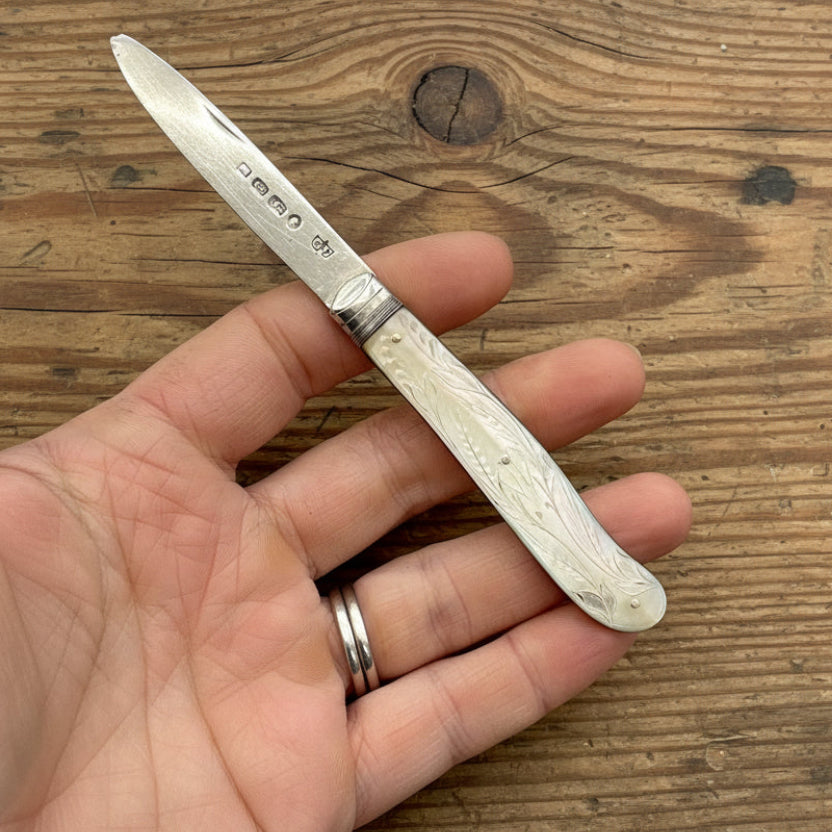 Hand holding a pocket knife with decorative handle on a wooden surface