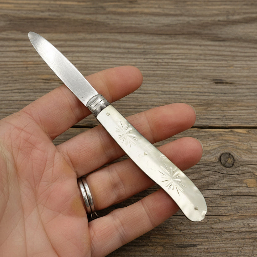 Hand holding a silver pocket knife with an engraved handle on a wooden surface