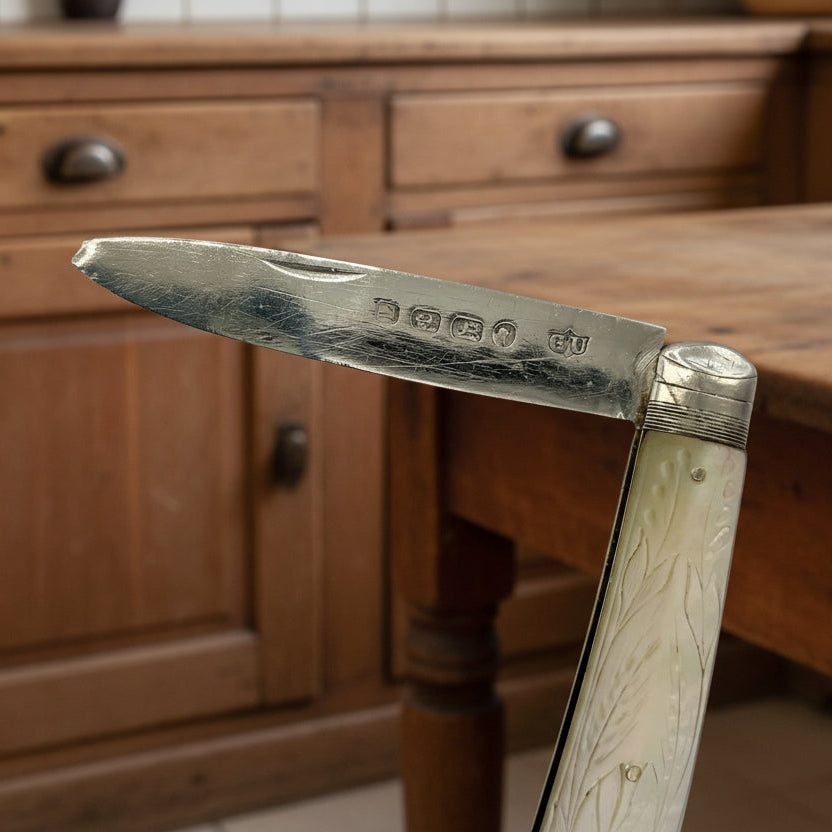 Close-up of the hallmarks on a blade of a folding knife with a pearl handle against a wooden background