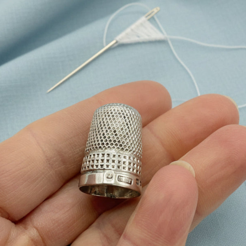 Silver thimble held in a hand against a needle and thread and material background