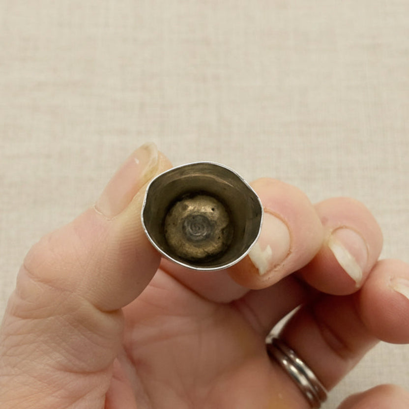 Hand holding a silver thimble with a beige material background