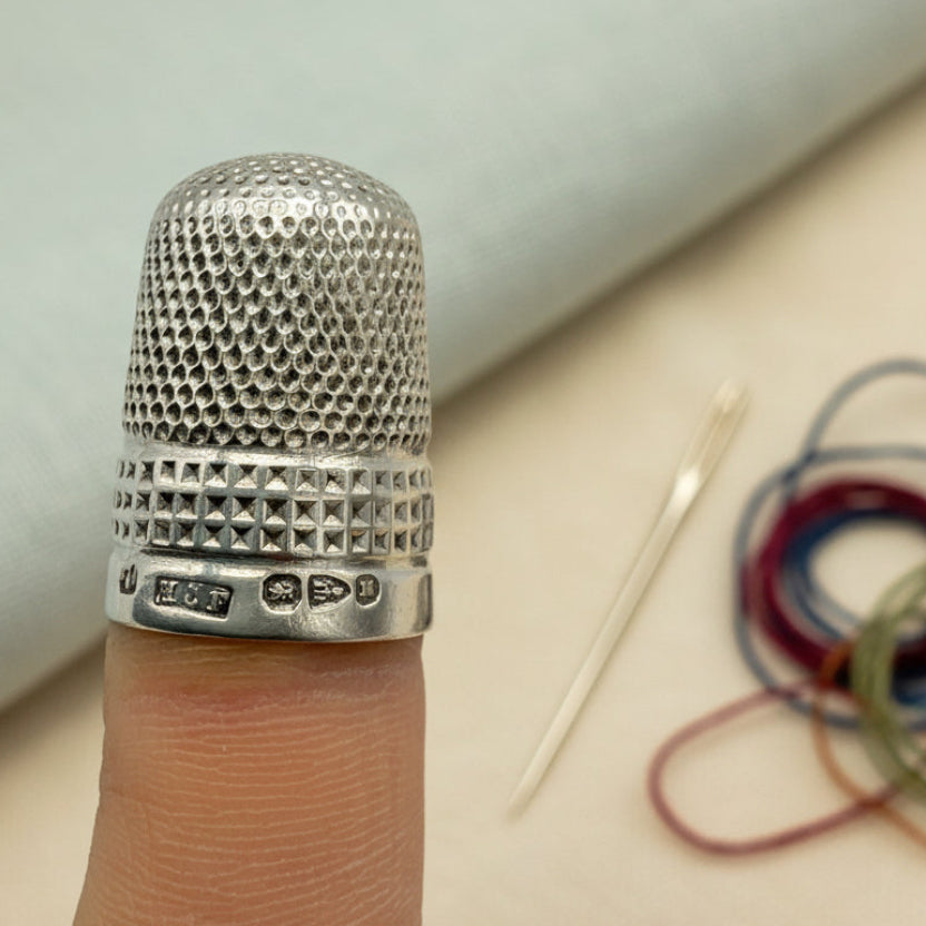 Silver thimble on a finger against a background with a needle and thread