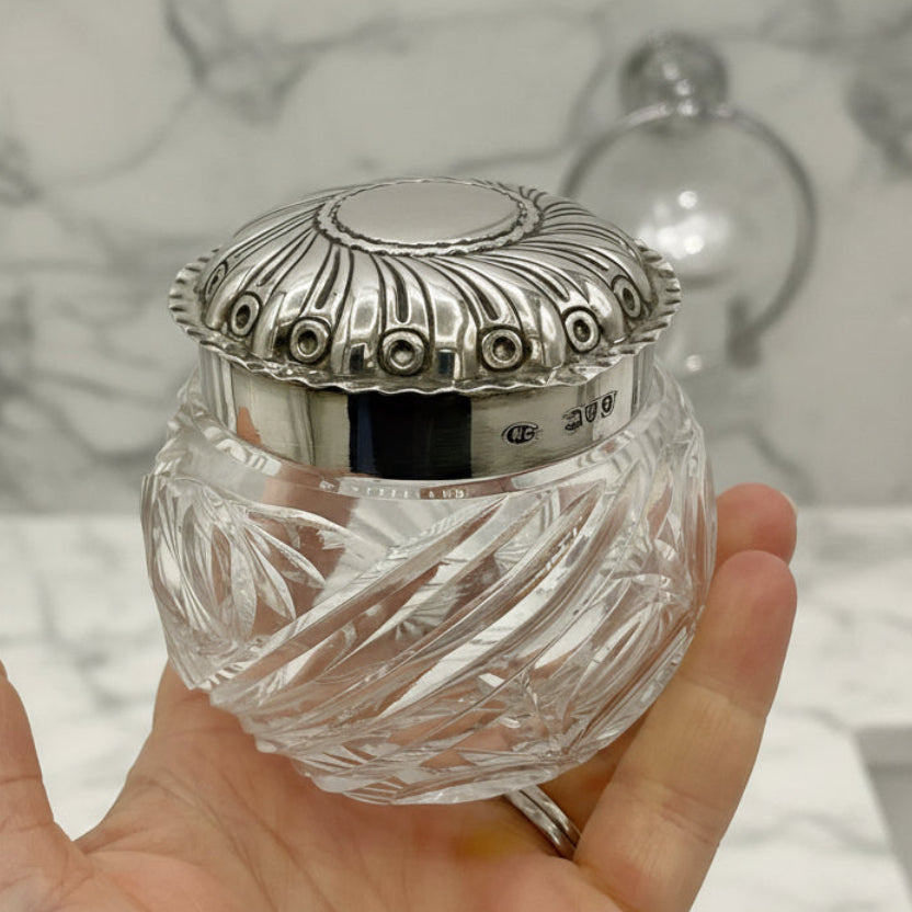 Hand holding a crystal jar with a silver lid against a white background