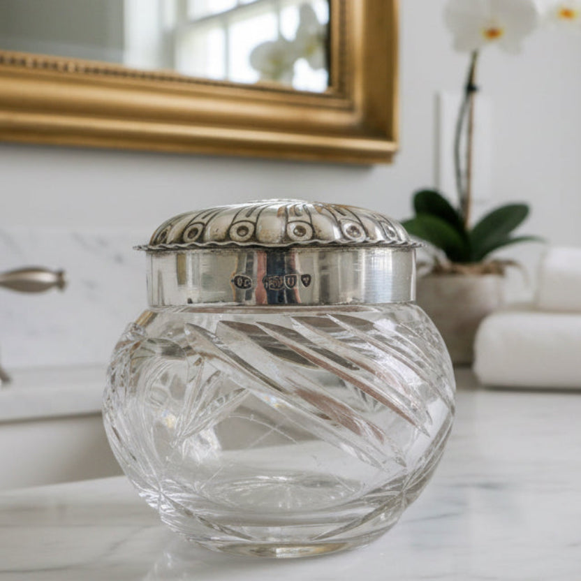 Decorative glass jar with silver lid on a marble surface, with a bathroom background.