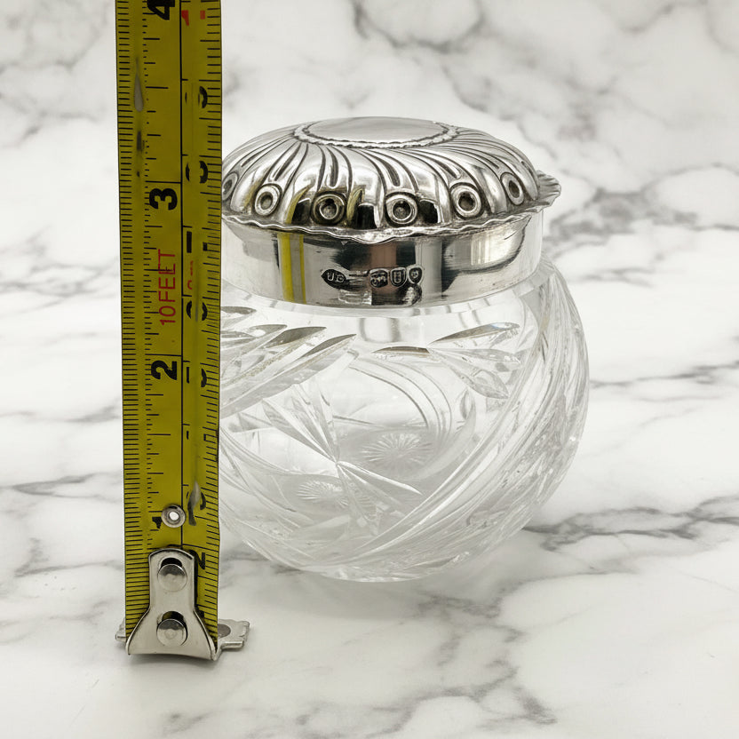 Clear glass jar with silver lid and decorative patterns, measured against a ruler on a marble background