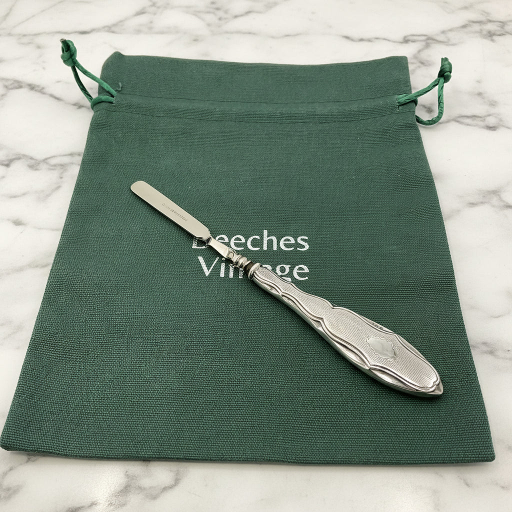 Silver cuticle pusher on a green drawstring bag with 'Beeches Vintage' branding on a marble surface.