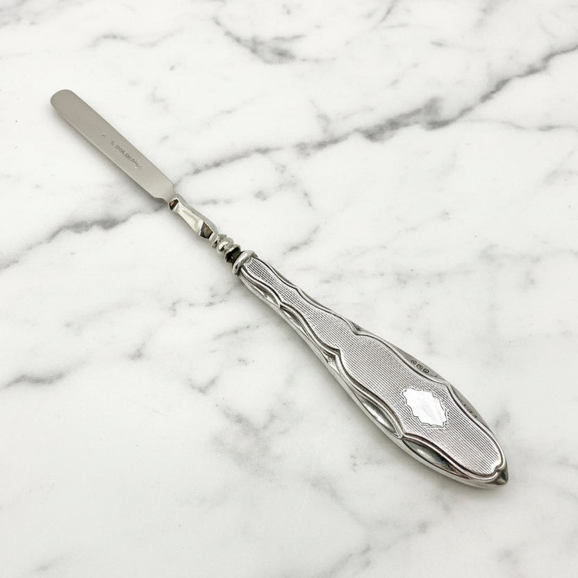 Silver cuticle pusher with decorative handle on a marble surface
