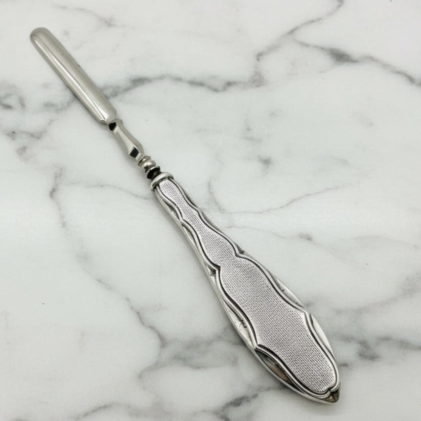 Silver cuticle pusher with decorative handle on a marble surface