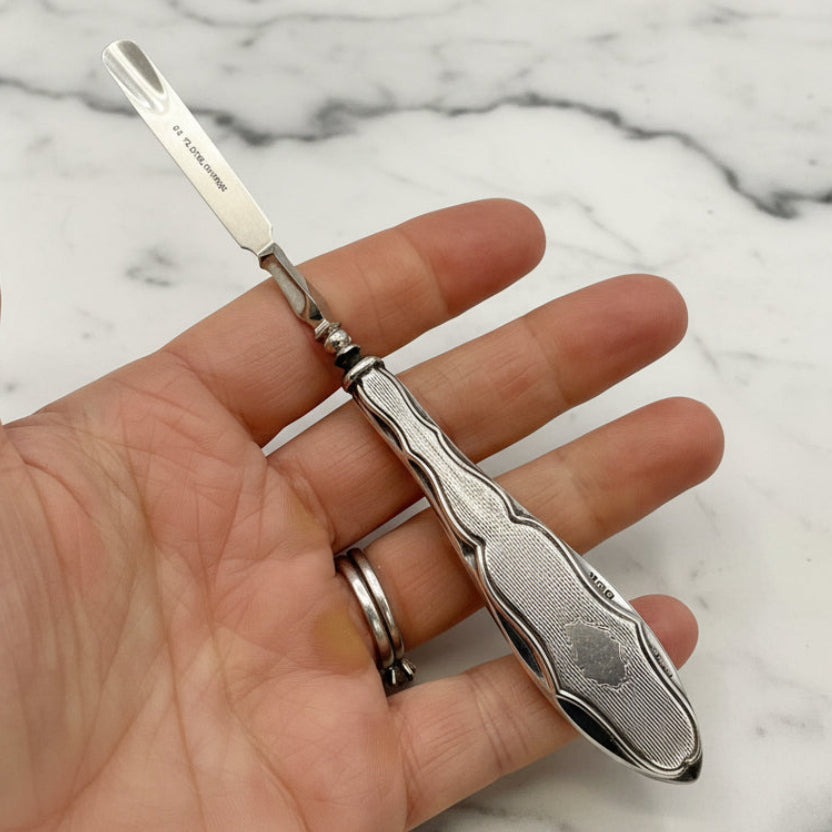Silver cuticle pusher held in a hand with a marble background
