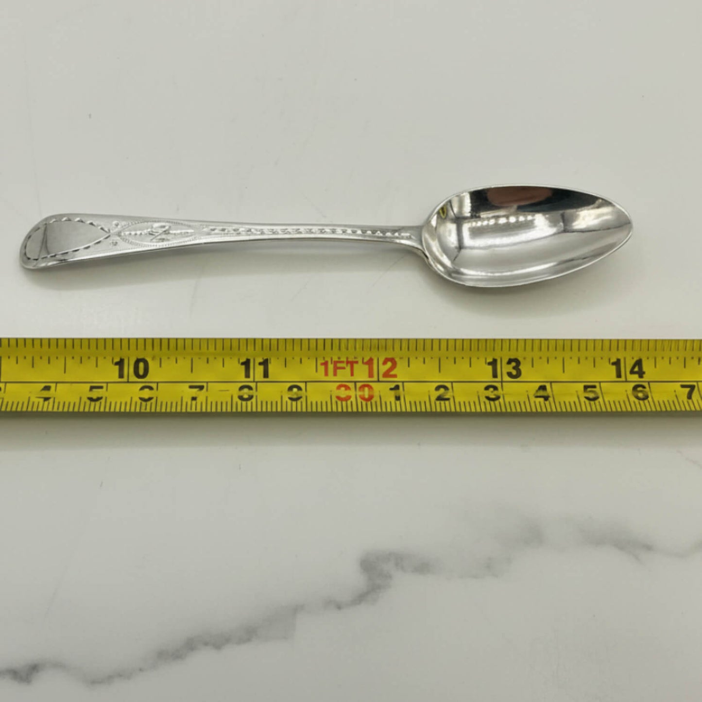 Antique Georgian sterling silver teaspoon with hallmarks from 1793, featuring intricate engraved details.