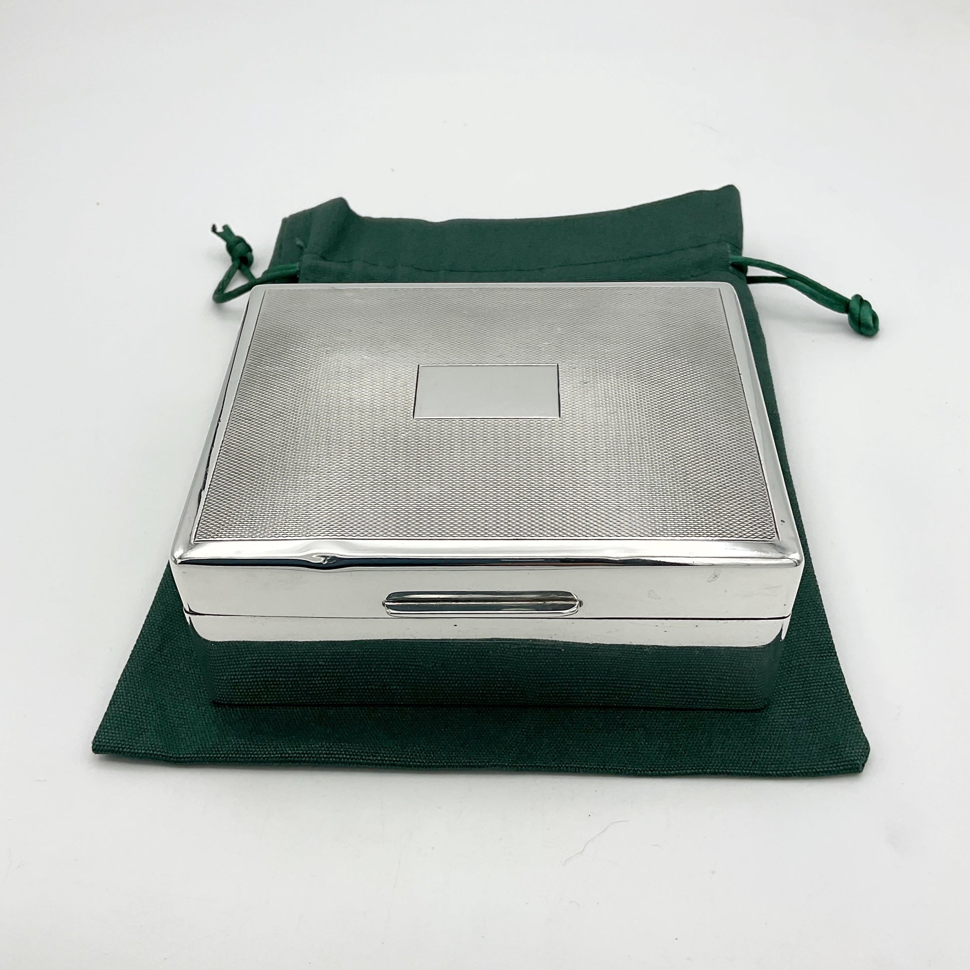 Solid silver cigarette box from the 1940s sitting on a green cotton gift bag