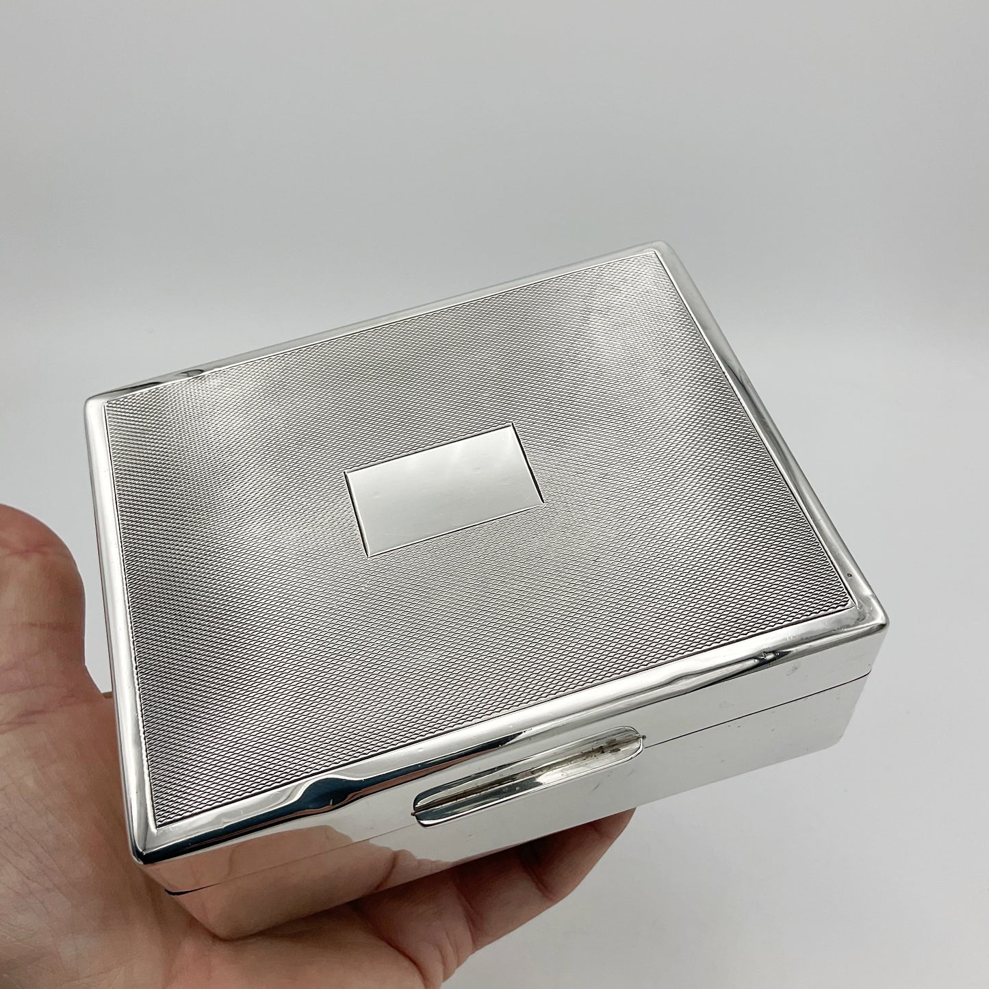 vintage silver cigarette box lid with blank cartouche in middle held in a hand