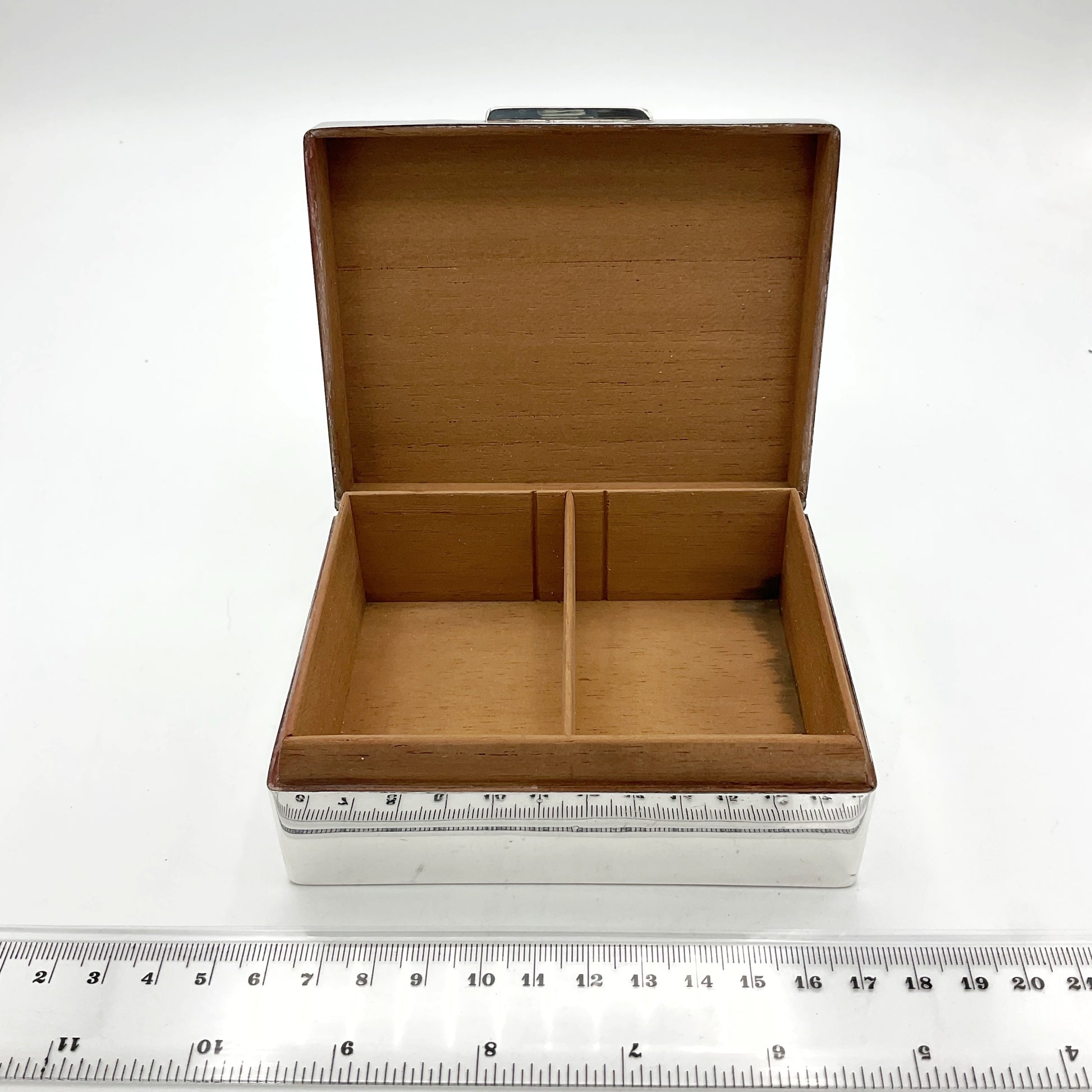 fully wood lined cigarette box with silver exterior next to ruler measuring approximately 10.5cm width