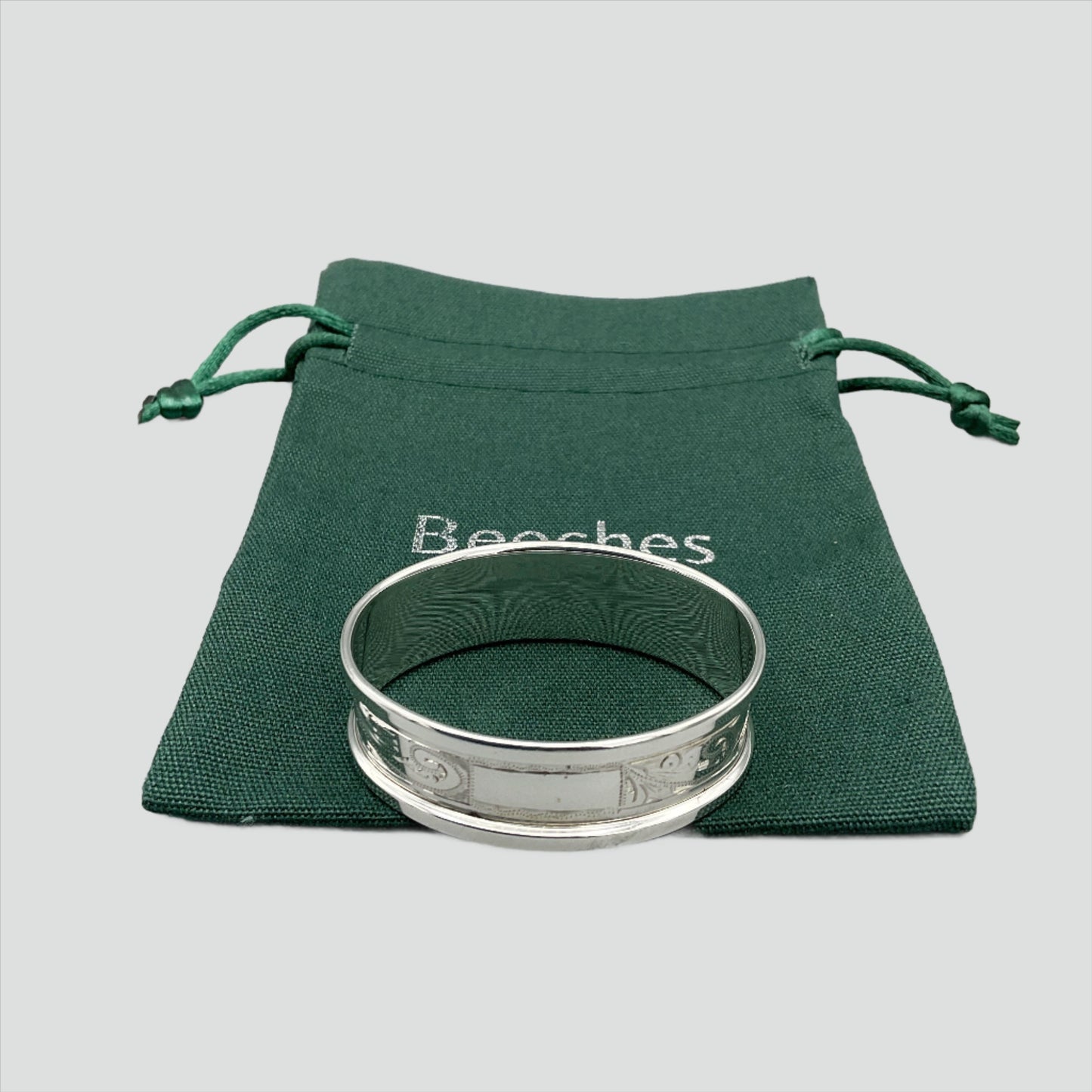 Engraved silver napkin ring sitting on a green cotton bag