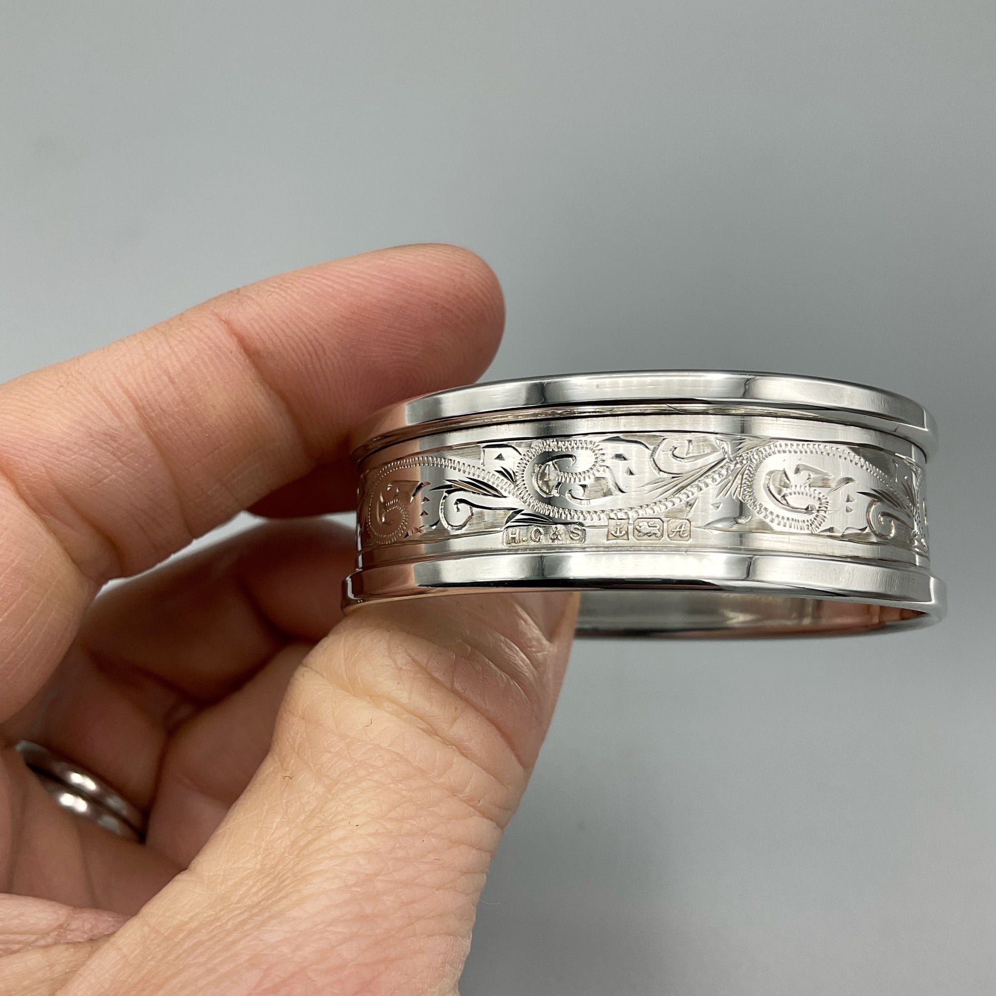 Engraved silver napkin ring showing the hallmarks and makers marks held in a hand