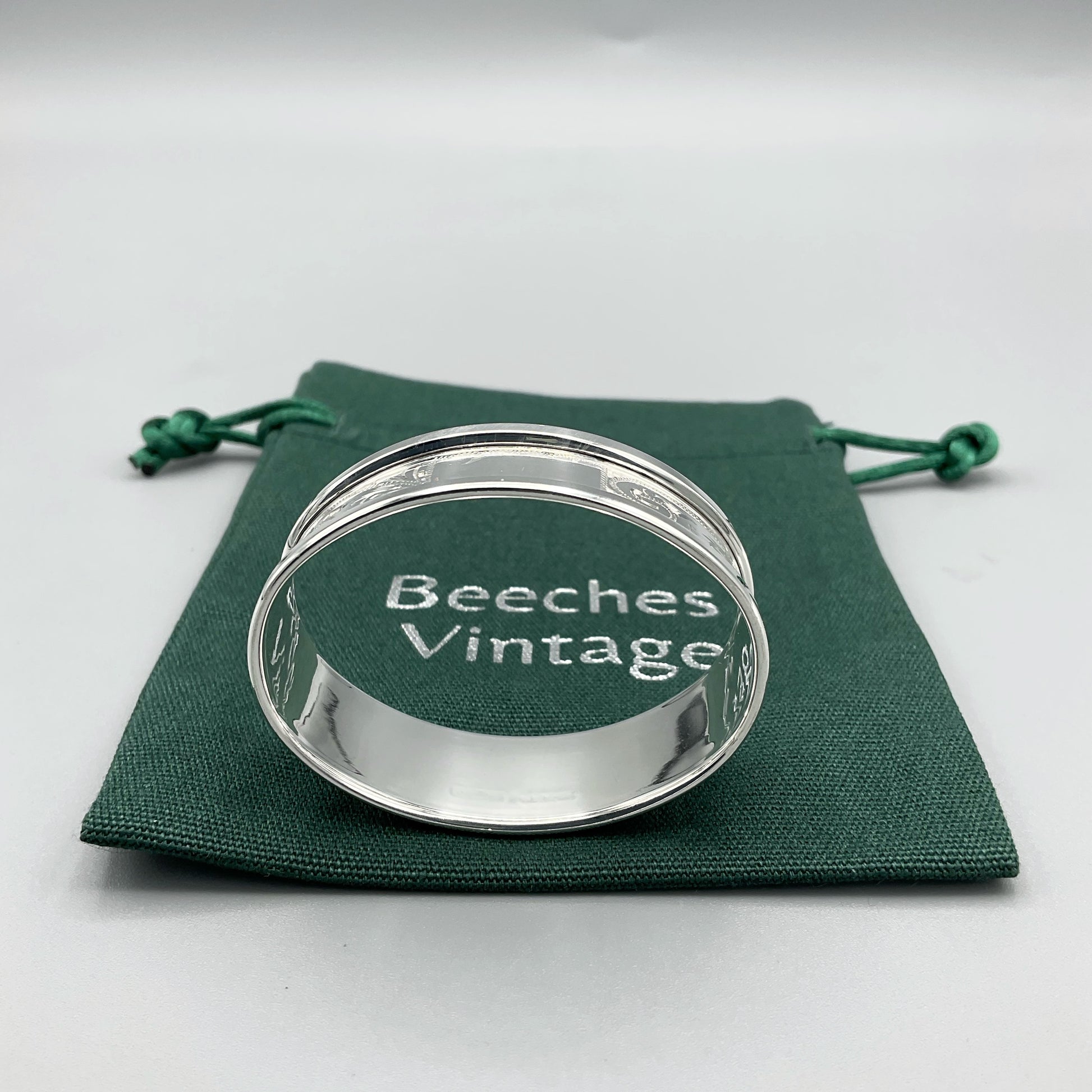 Engraved silver napkin ring sitting on a green cotton bag