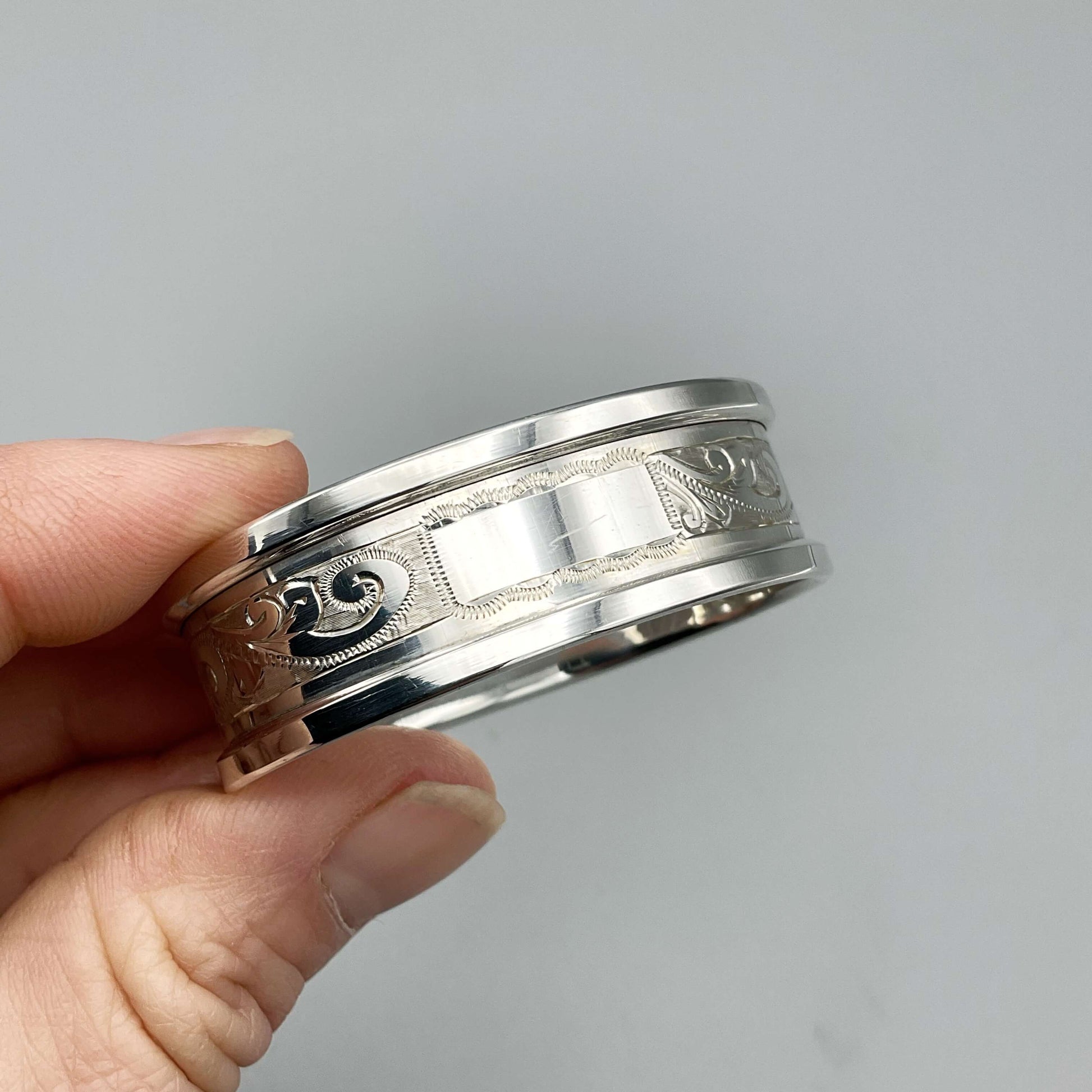Silver napkin ring with blank rectangular cartouche and etched flower pattern held in fingertips