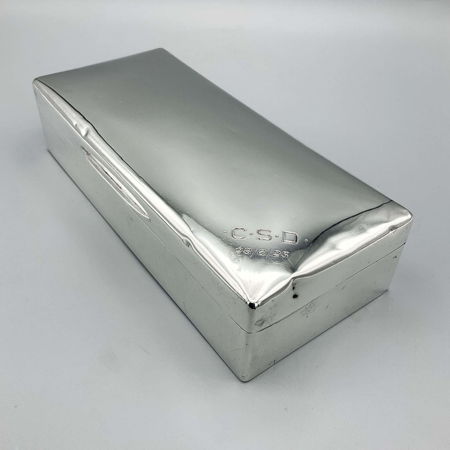 shiny silver rectangular cigarette box showing a corner with CSD engraved and 28/6/23