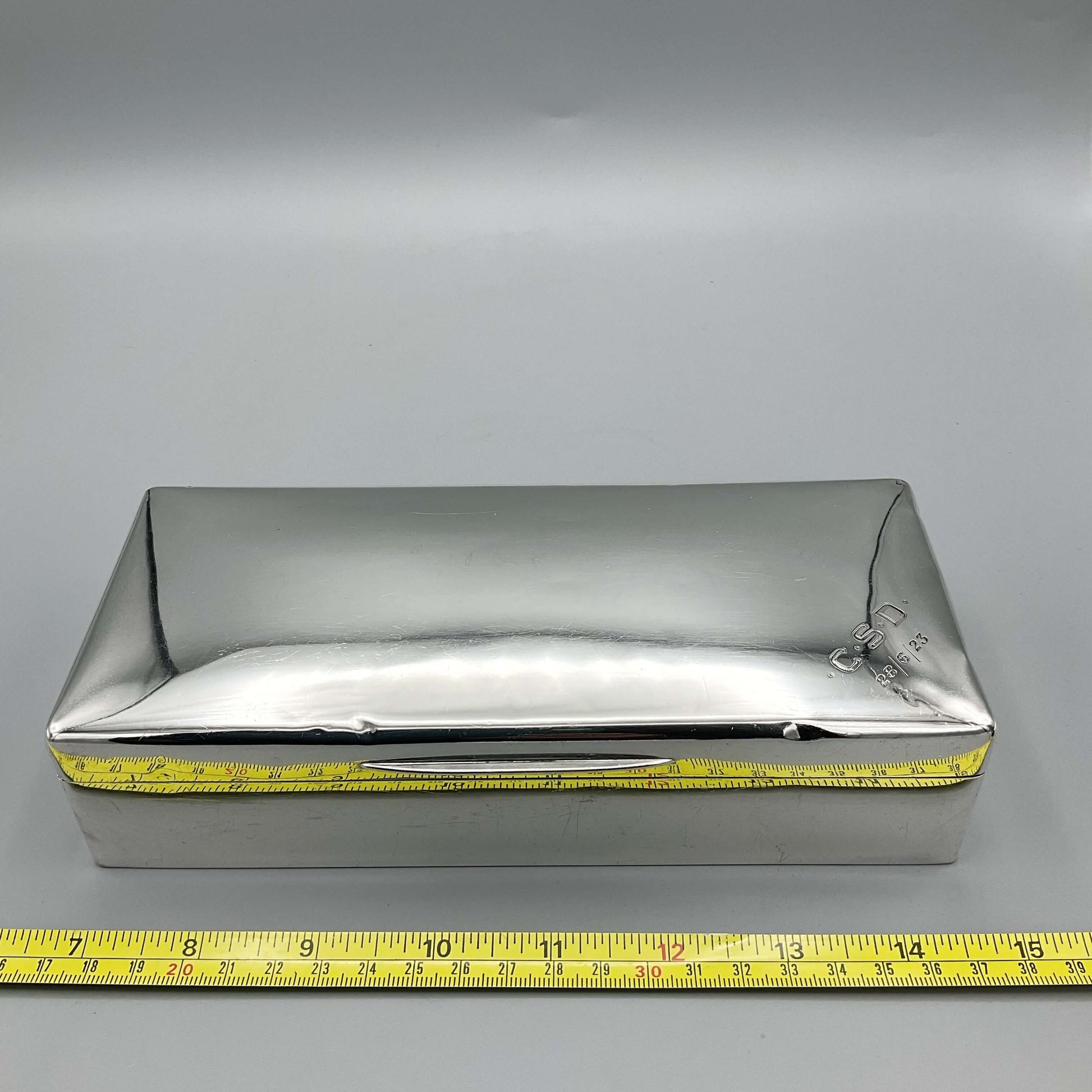 large shiny reflective silver cigarette box next to tape measure showing width as approx 21cm