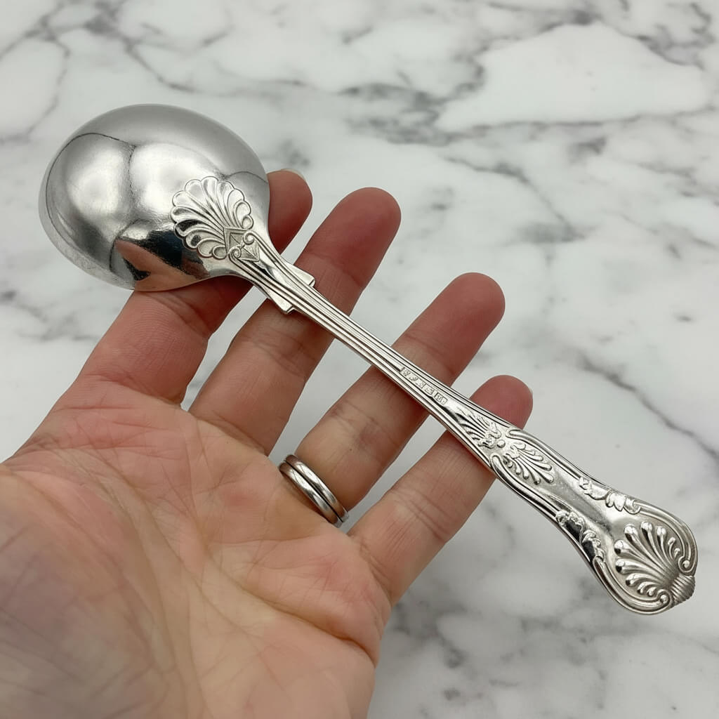 back of silver plated spoon held in a hand with a marble background