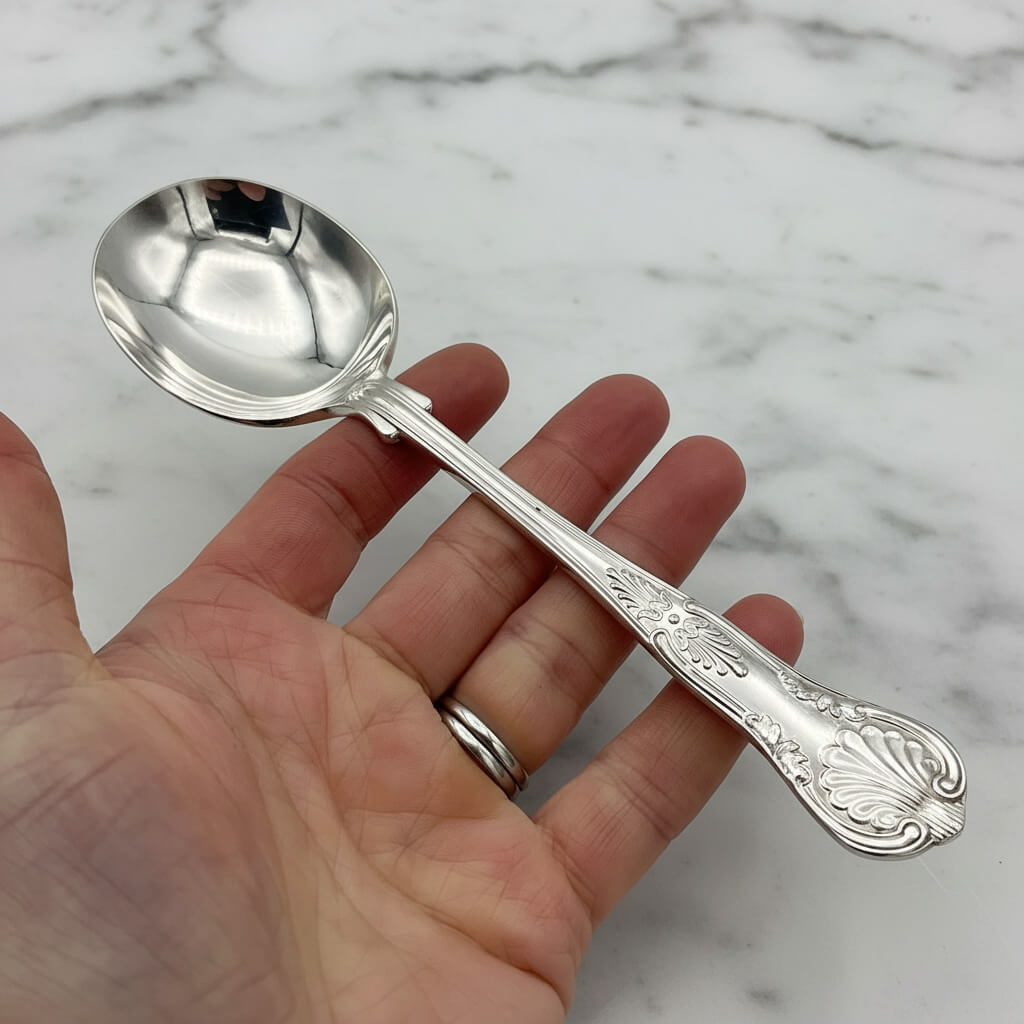 silver plated soup spoon held in a hand with a marble background